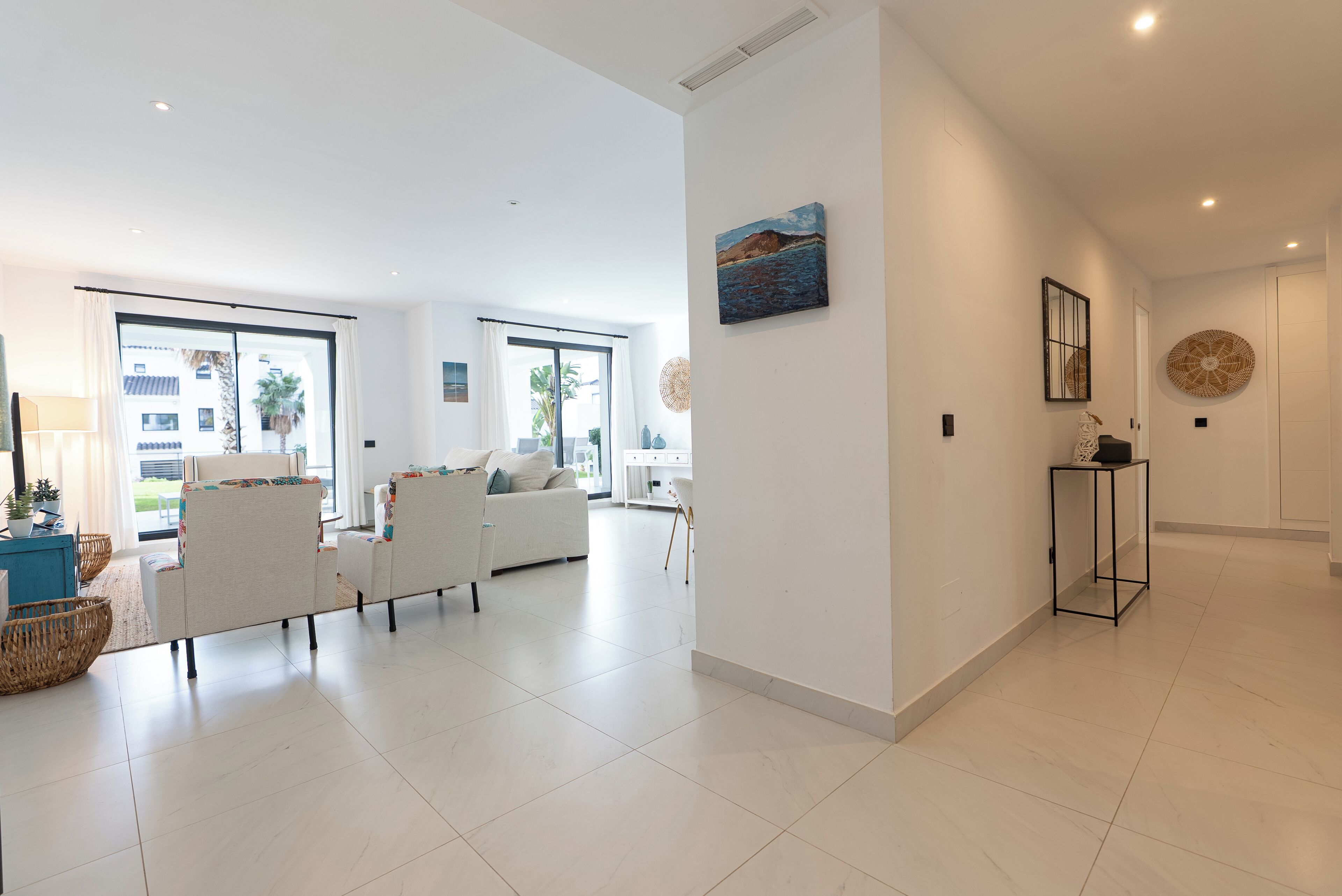 A spacious living room with a white sofa set, a coffee table, and a large window with curtains.