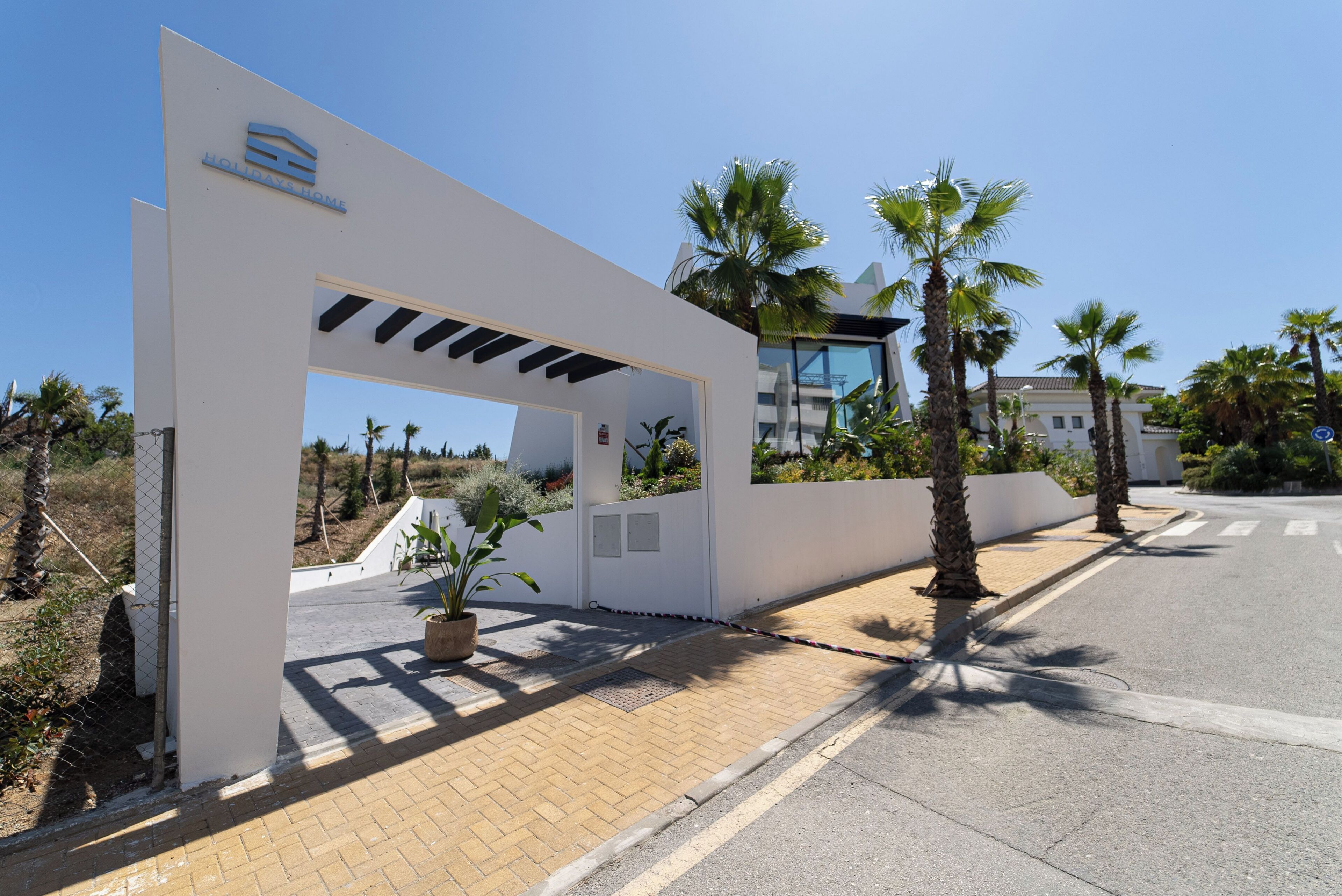 Ein moderner Hotel Eingangsbereich mit weißer Fassade, Palmen und blauem Himmel.