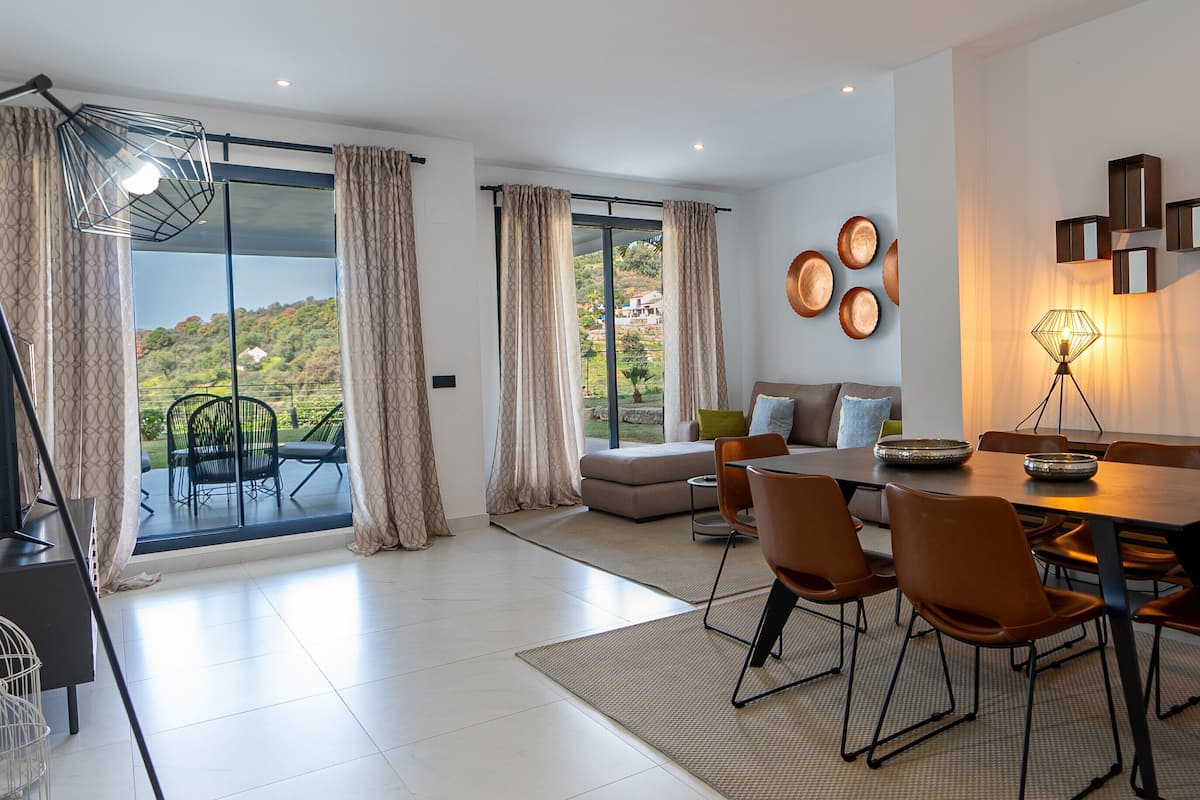 Un salon moderne avec un coin repas, de grandes fenêtres et une vue sur l’extérieur.