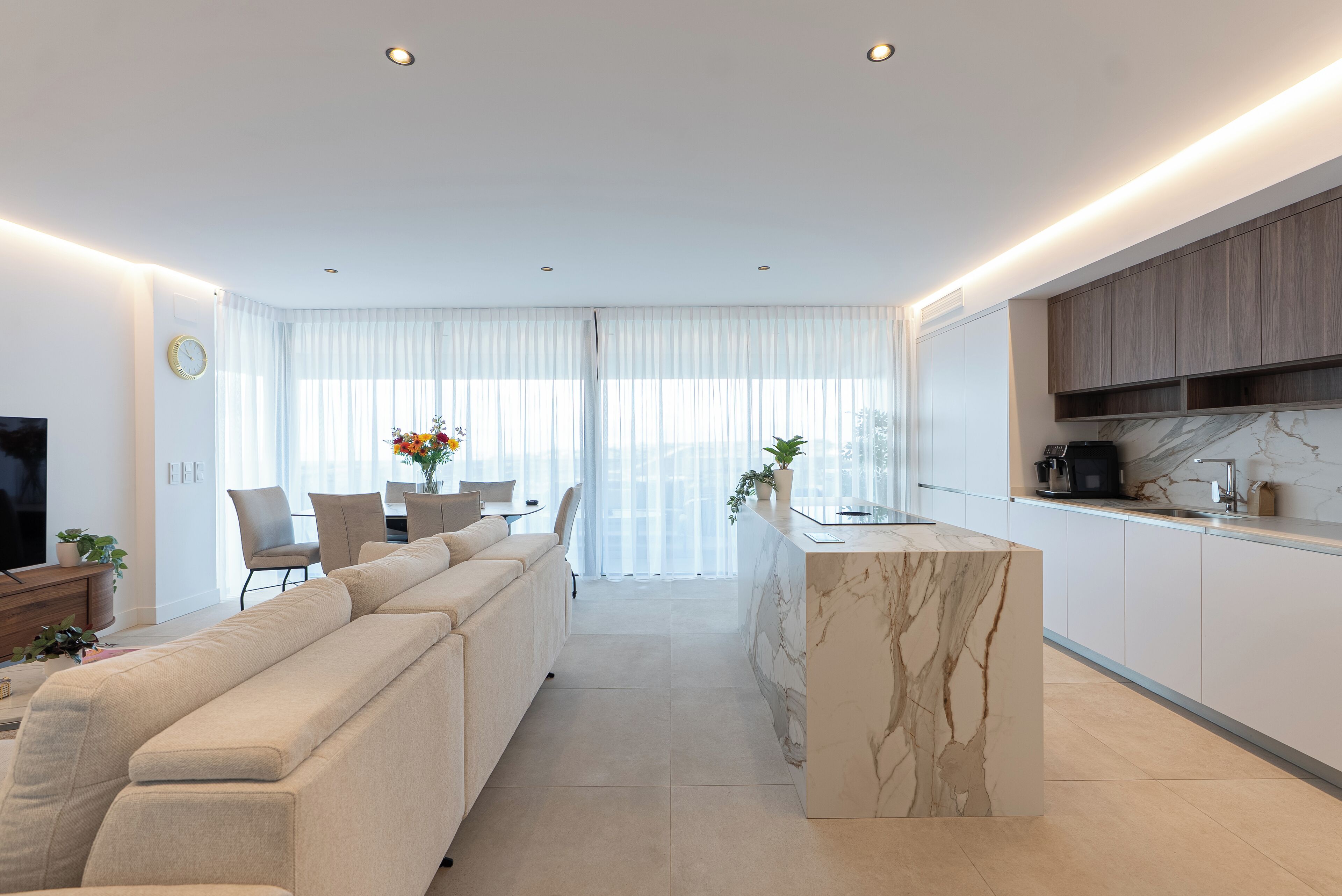 A modern living room with a sofa, a dining area with a table and chairs, and a kitchen with a marble island.
