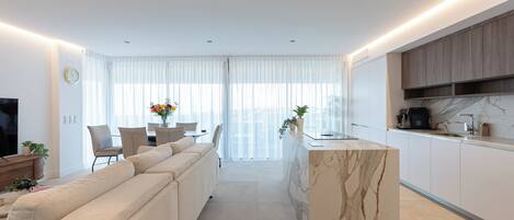 A modern living room with a sofa, a dining area with a table and chairs, and a kitchen with a marble island.