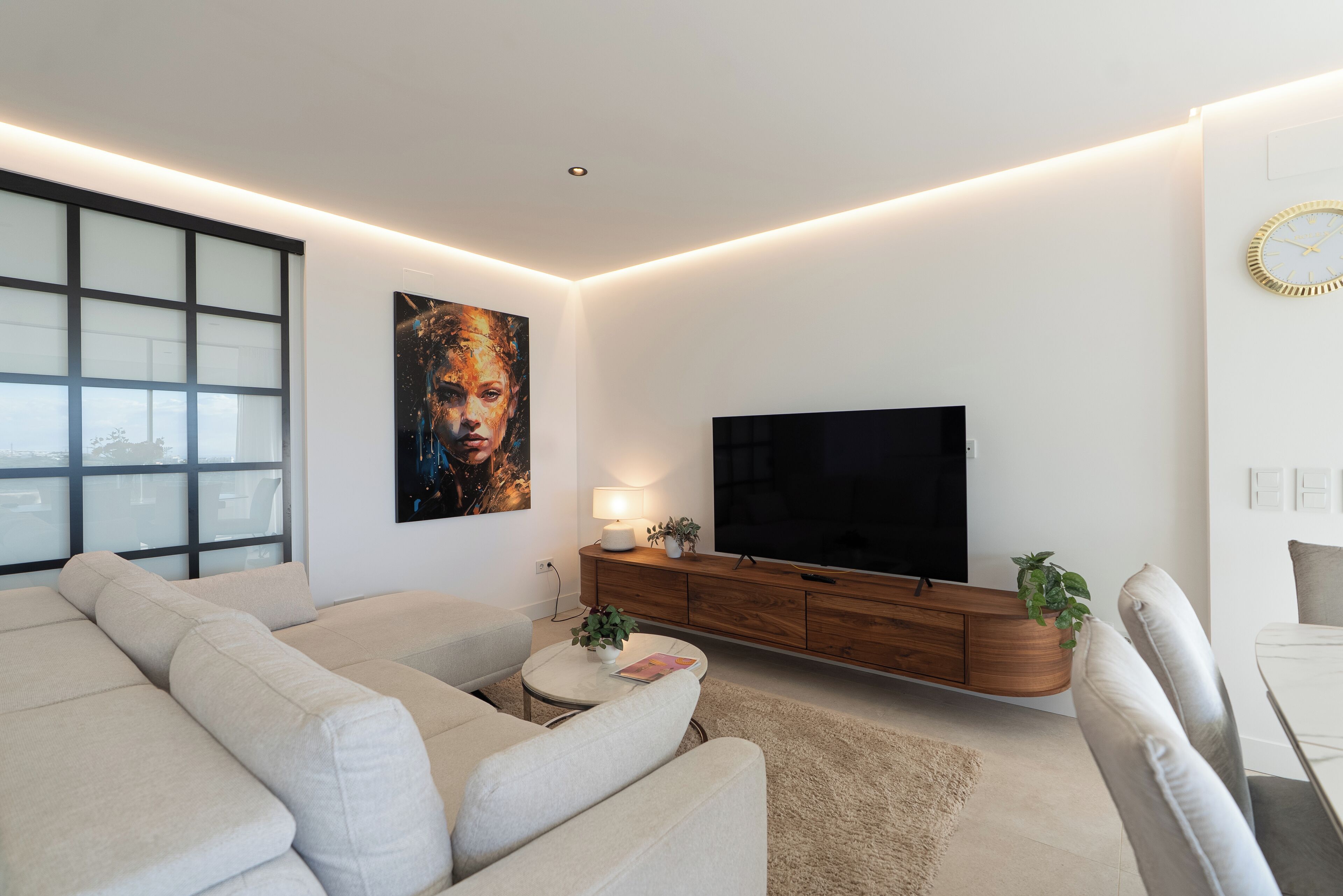 A modern living room with a sectional sofa, a flat-screen TV, a wooden console, and a large window.