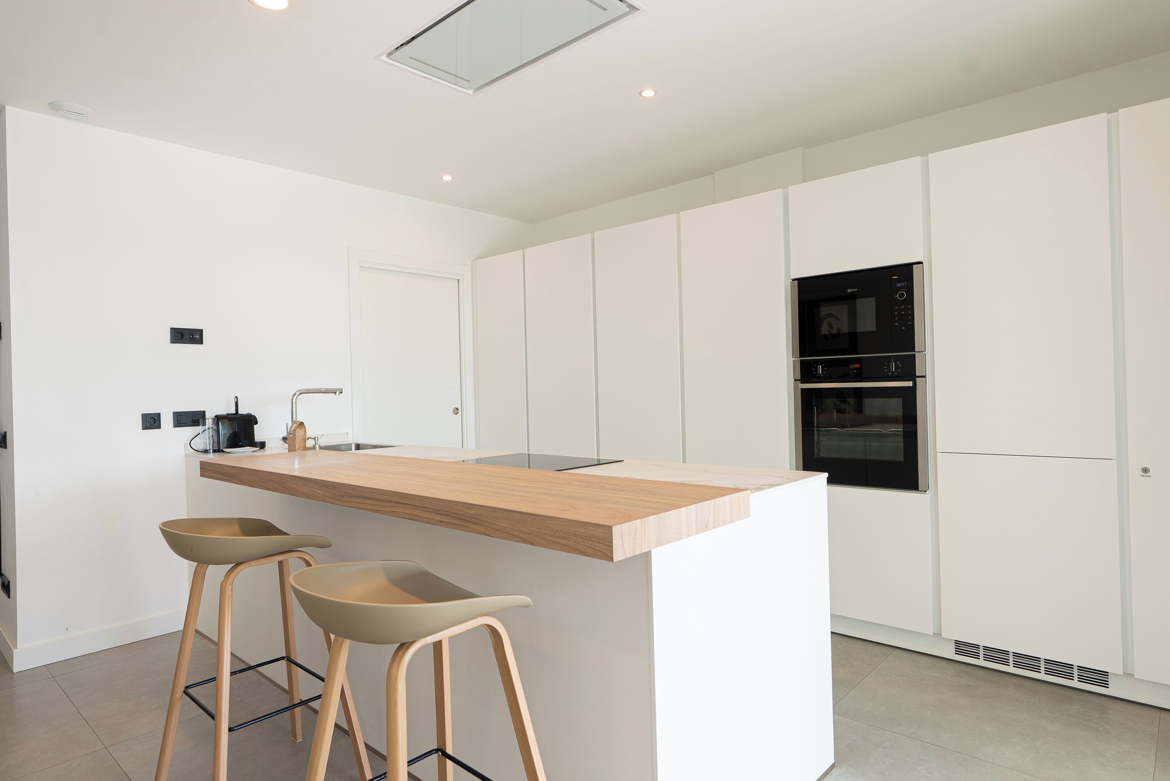 A modern kitchen with a central island, two bar stools, and built-in appliances.