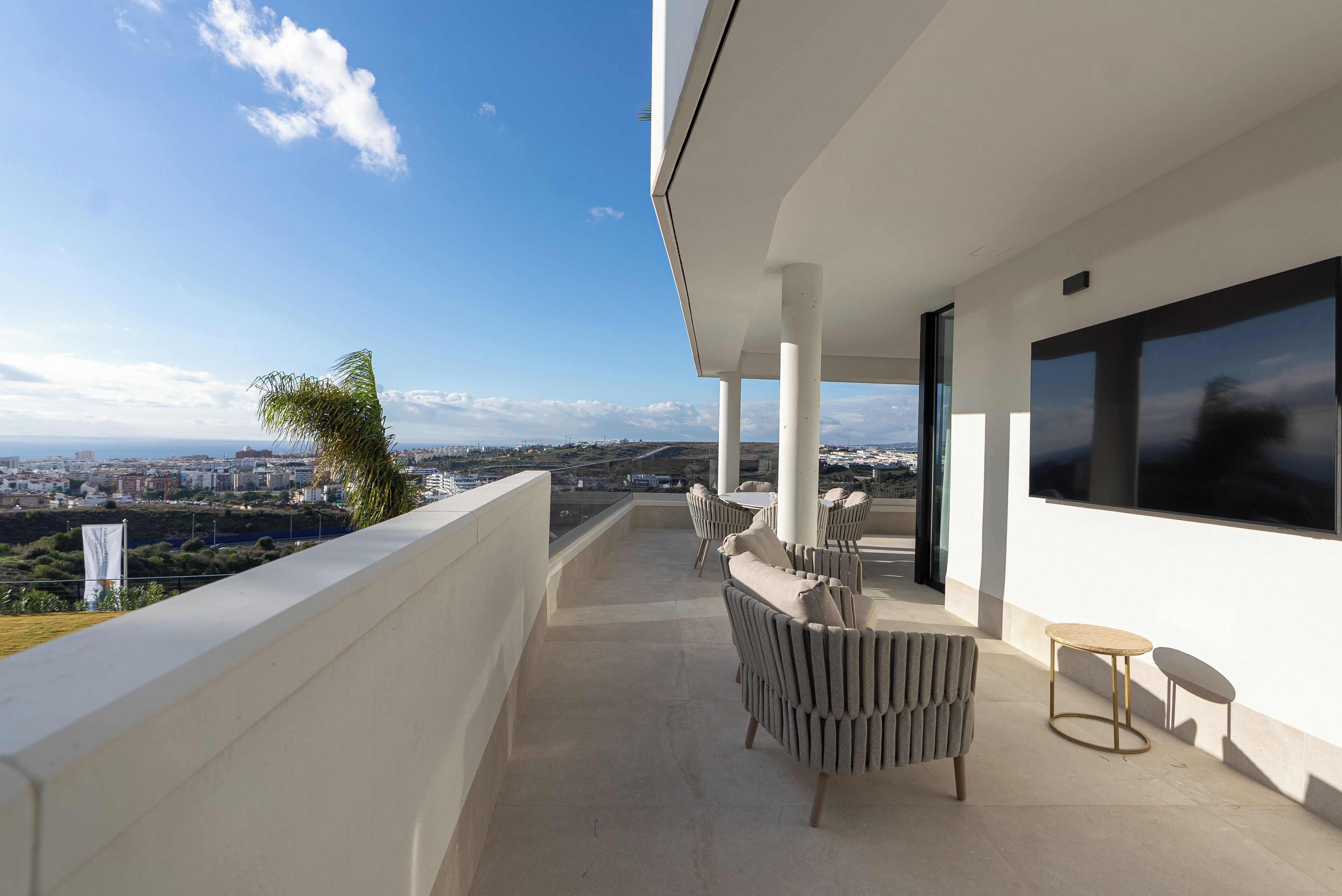 Un balcón moderno con vistas a un paisaje urbano, que incluye una zona de estar con un sofá y una mesita.