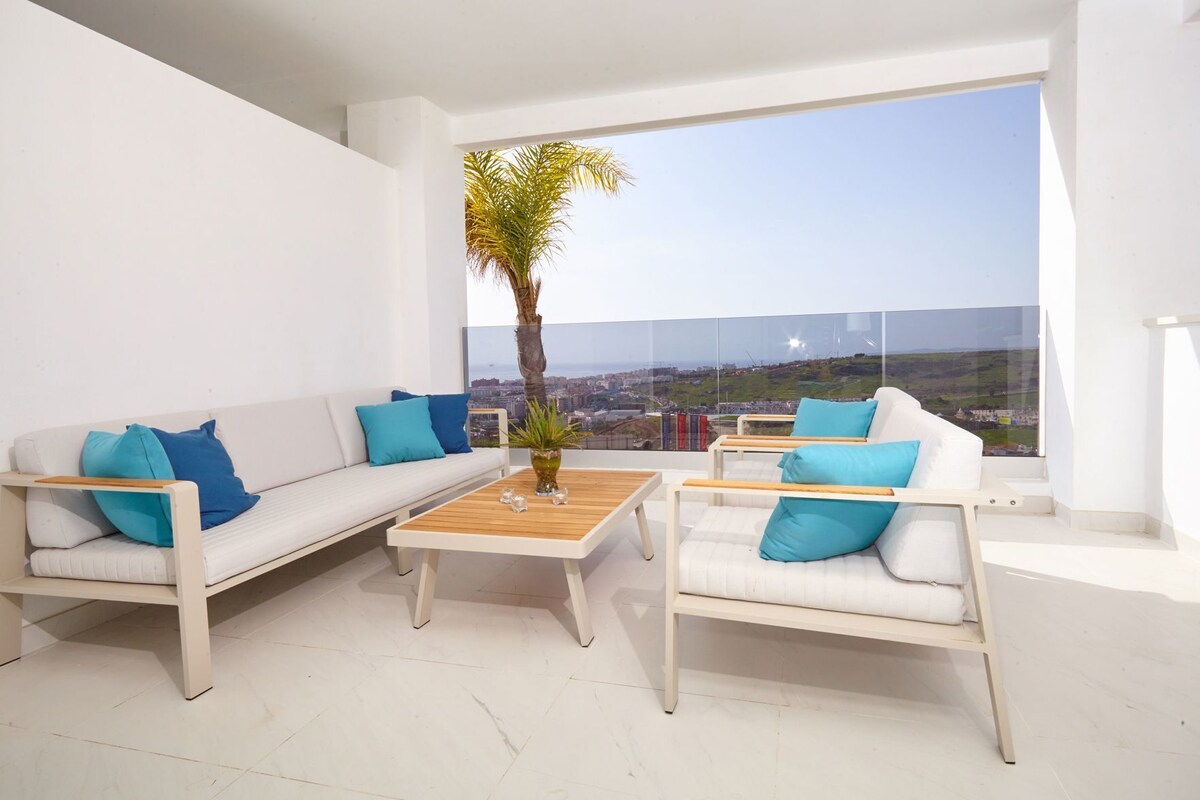 A modern living room with a white sofa, two armchairs, a coffee table, and a large window offering a city view.