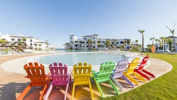 A poolside area with colorful Adirondack chairs, a clear blue sky, and modern buildings in the background.