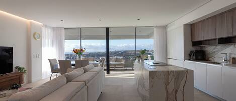 A modern living room with a sofa, a dining area, and a kitchen with a marble island.