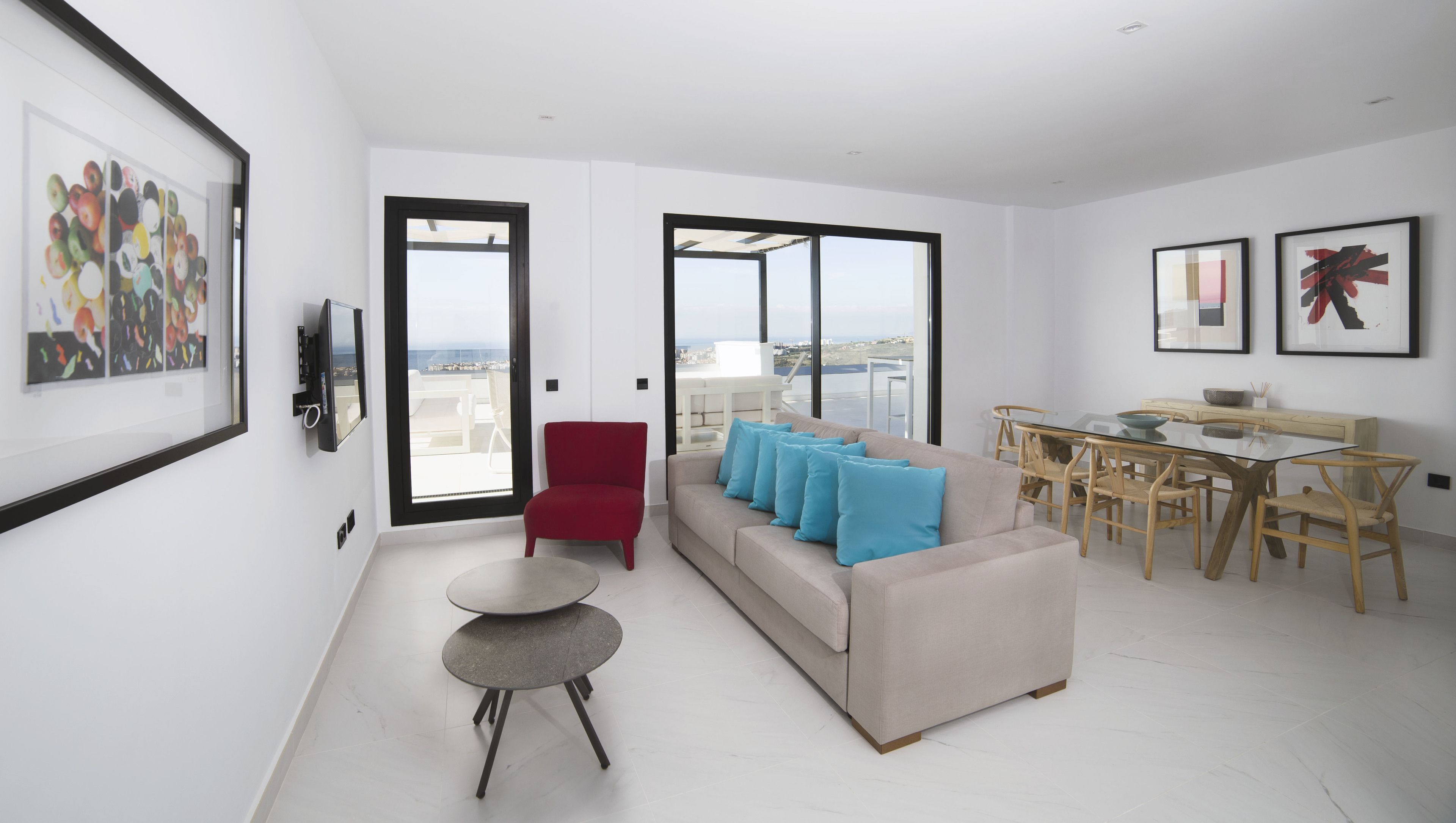 A modern living room with a sofa, red chair, dining table, and artwork on the walls.