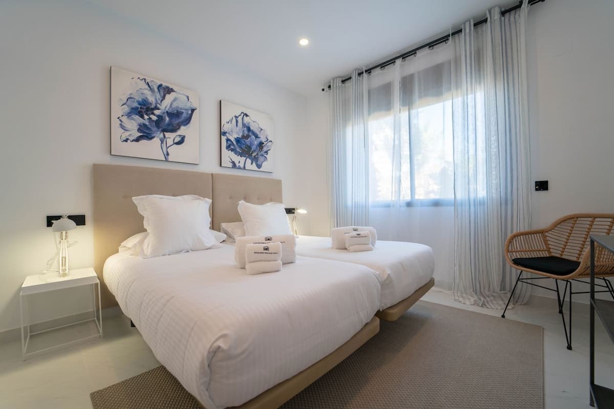 Une chambre moderne avec deux lits, du linge de lit blanc et des œuvres d’art accrochées au mur.