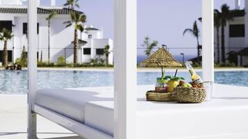Escena junto a la piscina con una sombrilla blanca, una botella de cerveza Corona y una cesta de frutas.