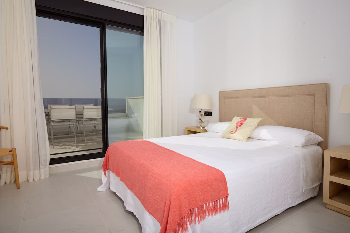 Une chambre d’hôtel avec un lit, une table de chevet, une lampe, une chaise et une vue sur l’extérieur, visible à travers une porte vitrée.