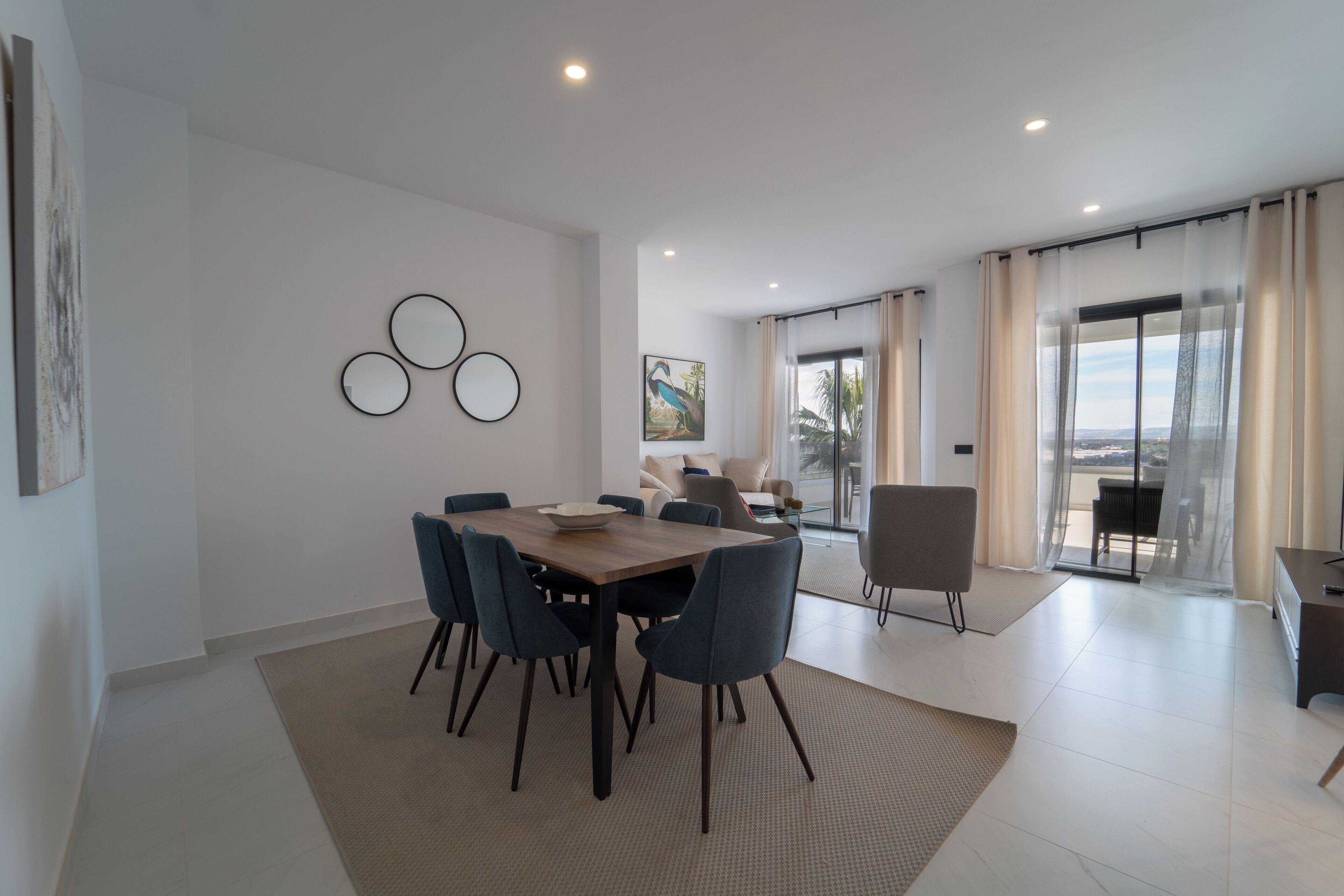 Un espace repas moderne avec une table et des chaises en bois, une grande fenêtre avec des rideaux et une vue sur l’extérieur.