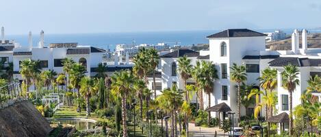 Un complexe hôtelier avec des bâtiments blancs, des palmiers, une piscine et une vue sur la mer.