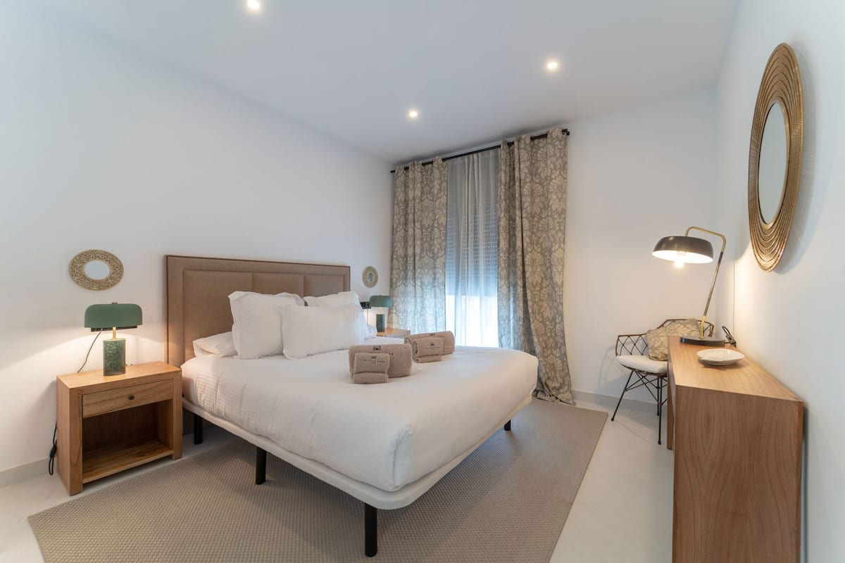Une chambre d’hôtel moderne équipée d’un lit, d’une table de chevet, d’une lampe et d’un bureau avec une chaise.