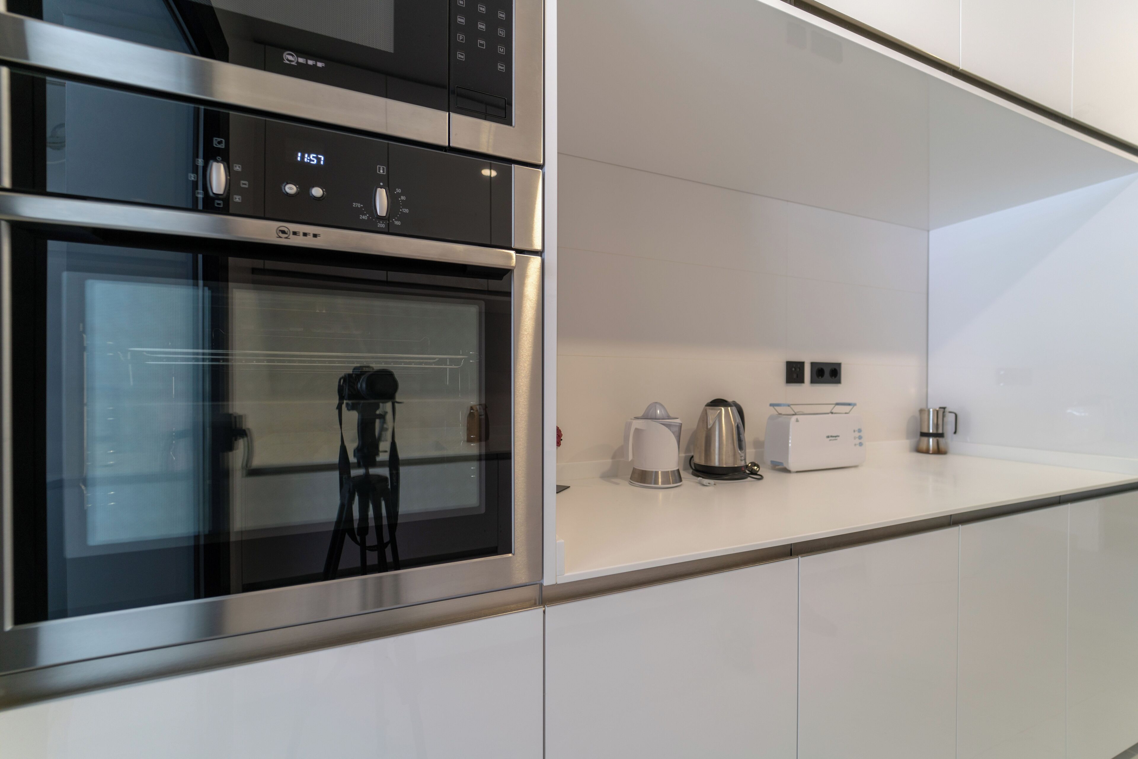 Una cocina moderna con horno empotrado y microondas, además de cafetera y tostadora sobre la encimera.
