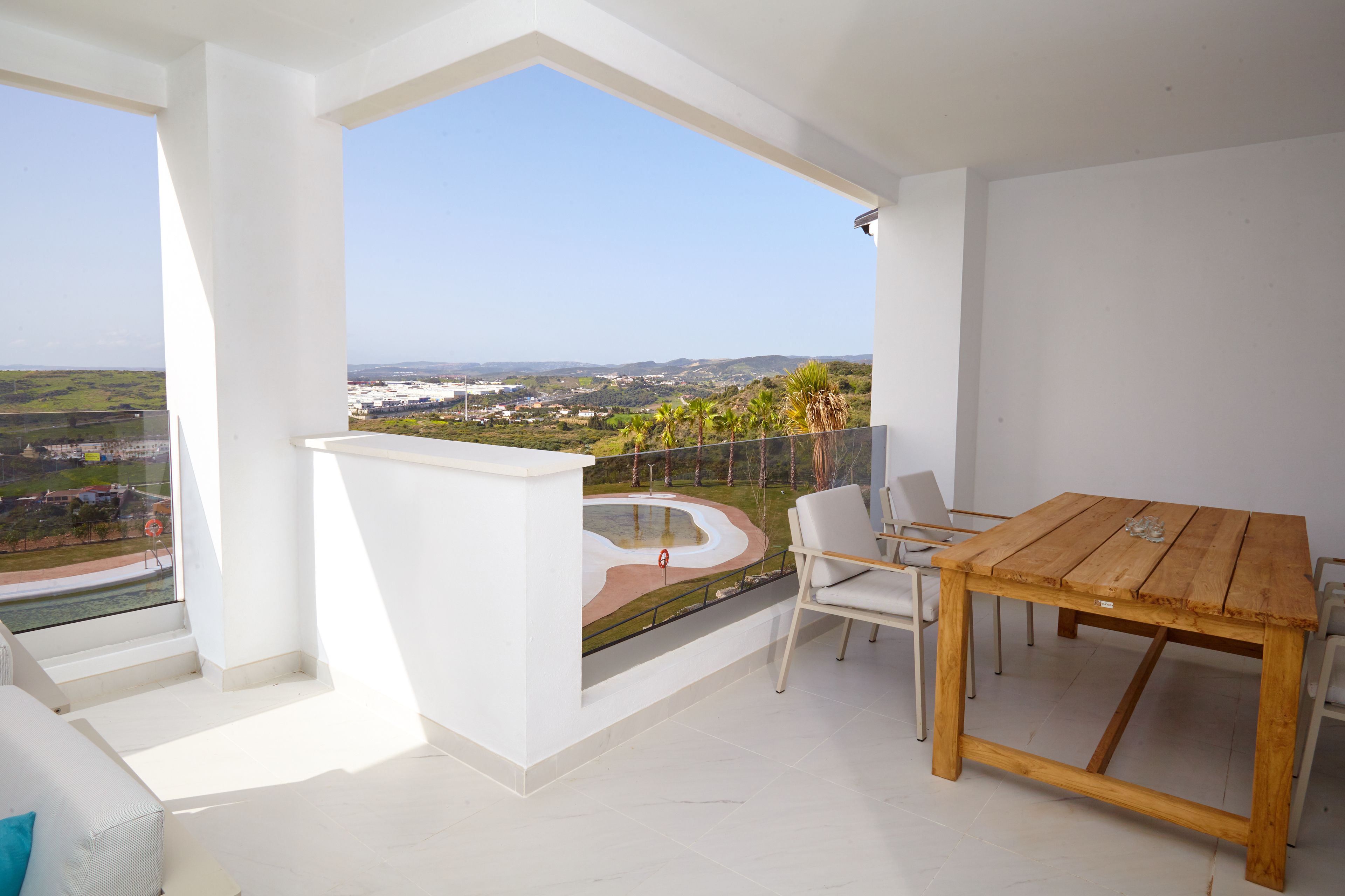 Ein Balkon mit Holztisch und -stühlen, der Blick auf eine Küstenlandschaft bietet.