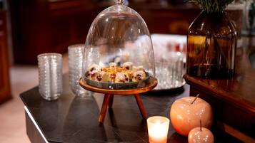 A dessert display with a glass dome, candles, and a vase with greenery on a wooden table.