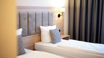 Una habitación de hotel con una cama, dos almohadas, una mesita de noche, una lámpara de pared y una cortina.