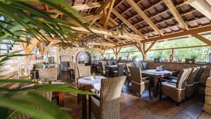 A rustic wooden dining area with brick walls and large windows. Tables and wicker chairs are arranged for dining. - Korbstadthotel Krone (Lichtenfels)