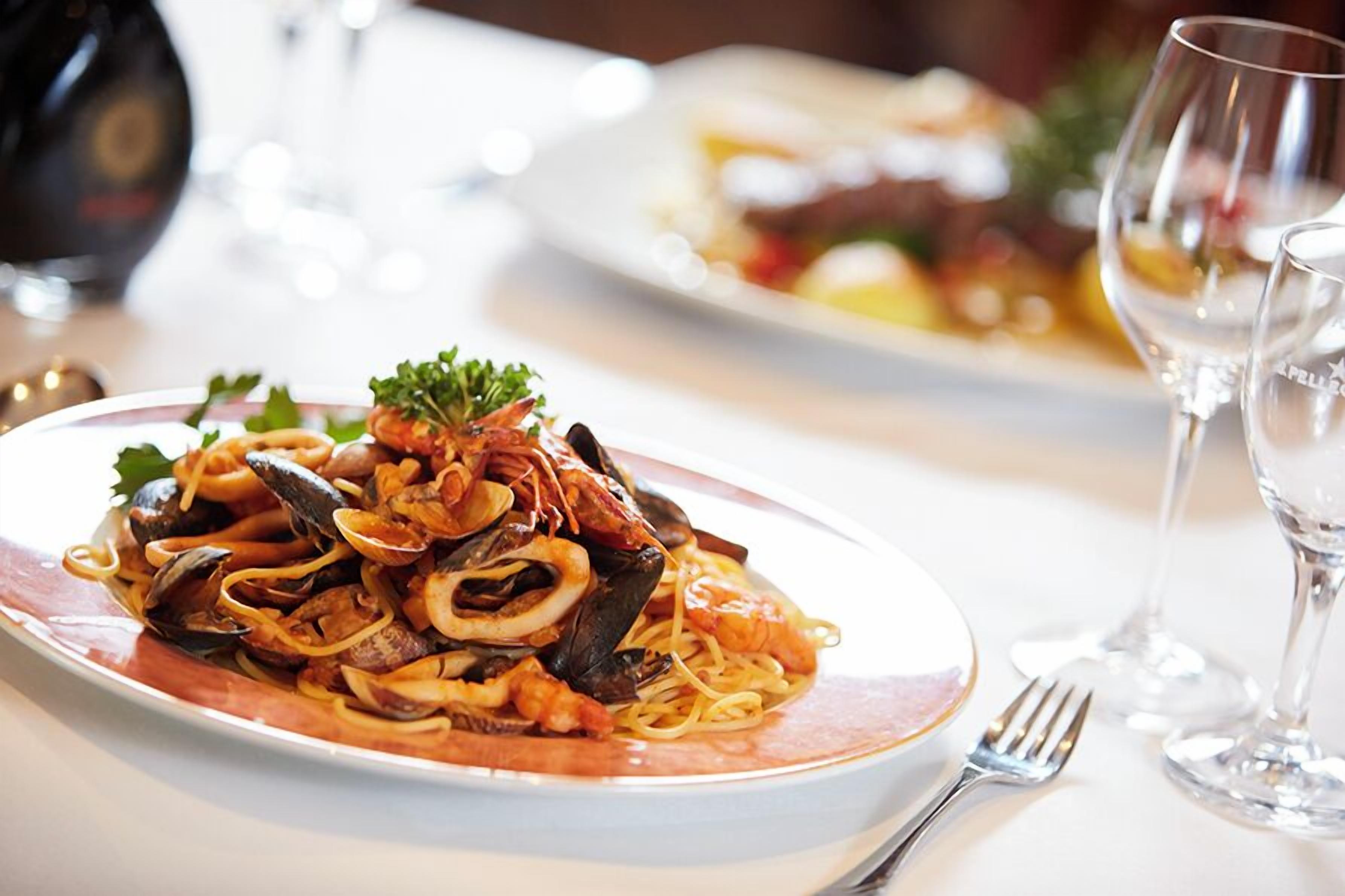 Un plato de pasta con mariscos, un tenedor y una copa de vino cerca.