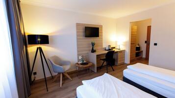 Quarto de hotel com cama, escrivaninha, cadeira e televisão fixada na parede.