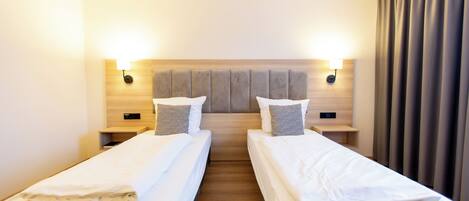 Una habitación de hotel con dos camas individuales, cabecero de madera, lámparas de noche y una cortina.
