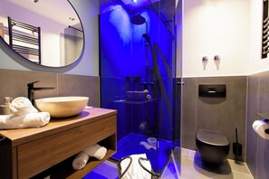 A modern bathroom with a round mirror, wooden vanity, a large bowl sink, a glass-enclosed shower, and a toilet. - Korbstadthotel Krone (Lichtenfels)
