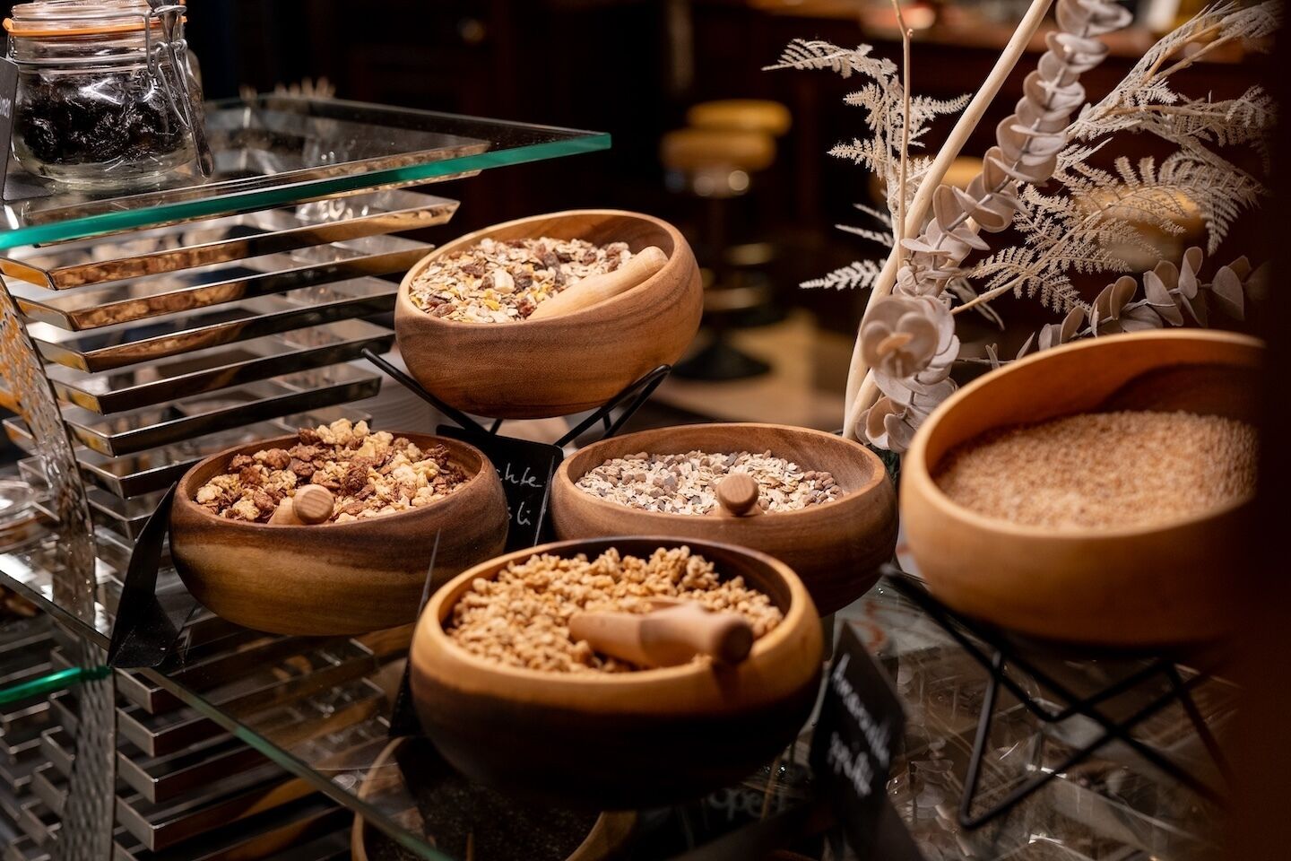 A display of various grains and seeds in wooden bowls on a glass shelf.