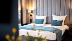 A modern hotel room with a large bed, two pillows, a bedside table with a lamp, and a wall-mounted panel. - Korbstadthotel Krone (Lichtenfels)