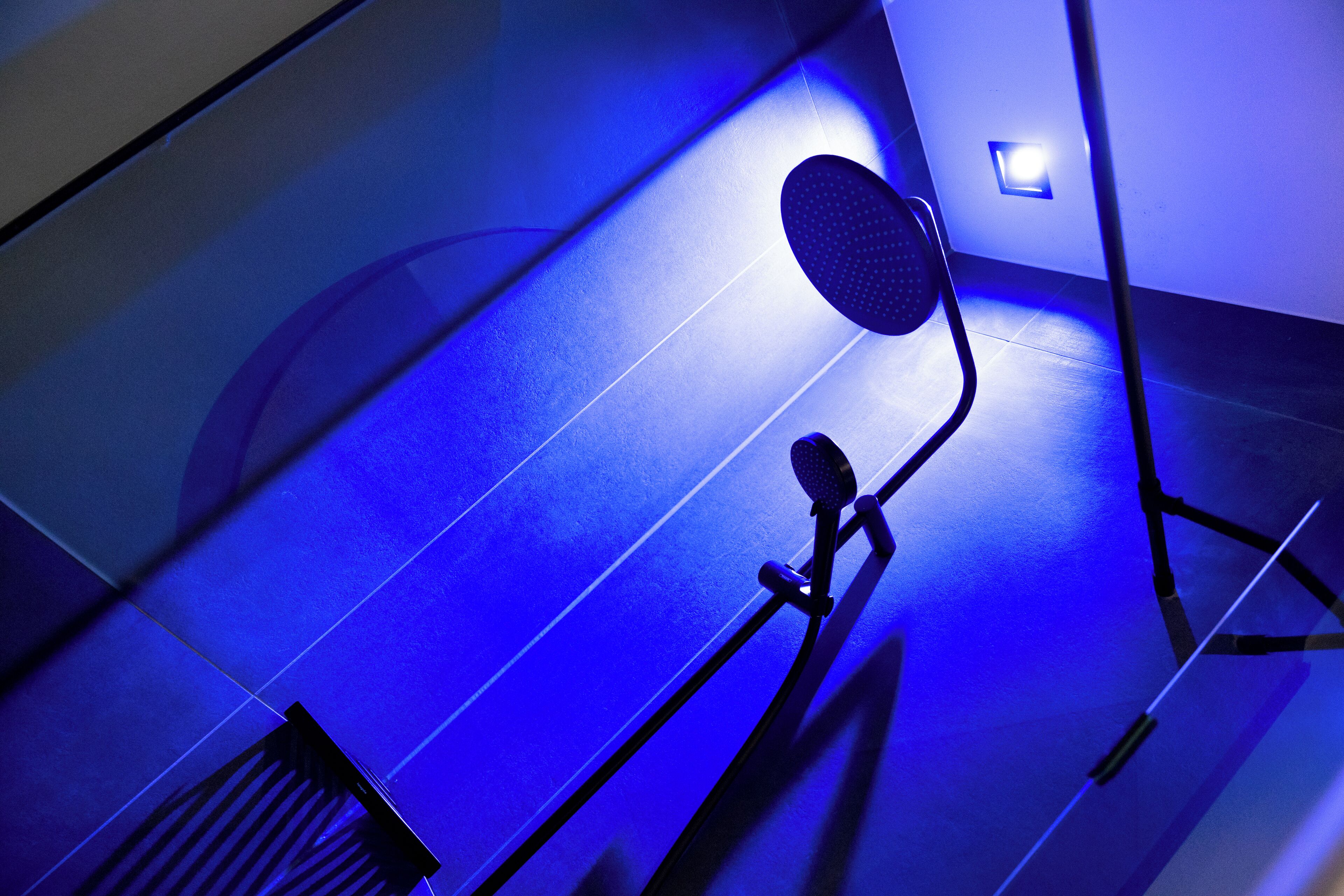 A blue-lit stairwell with a handrail and a wall-mounted light fixture.