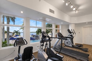 A gym with cardio machines, large windows, and a view of a pool and palm trees.