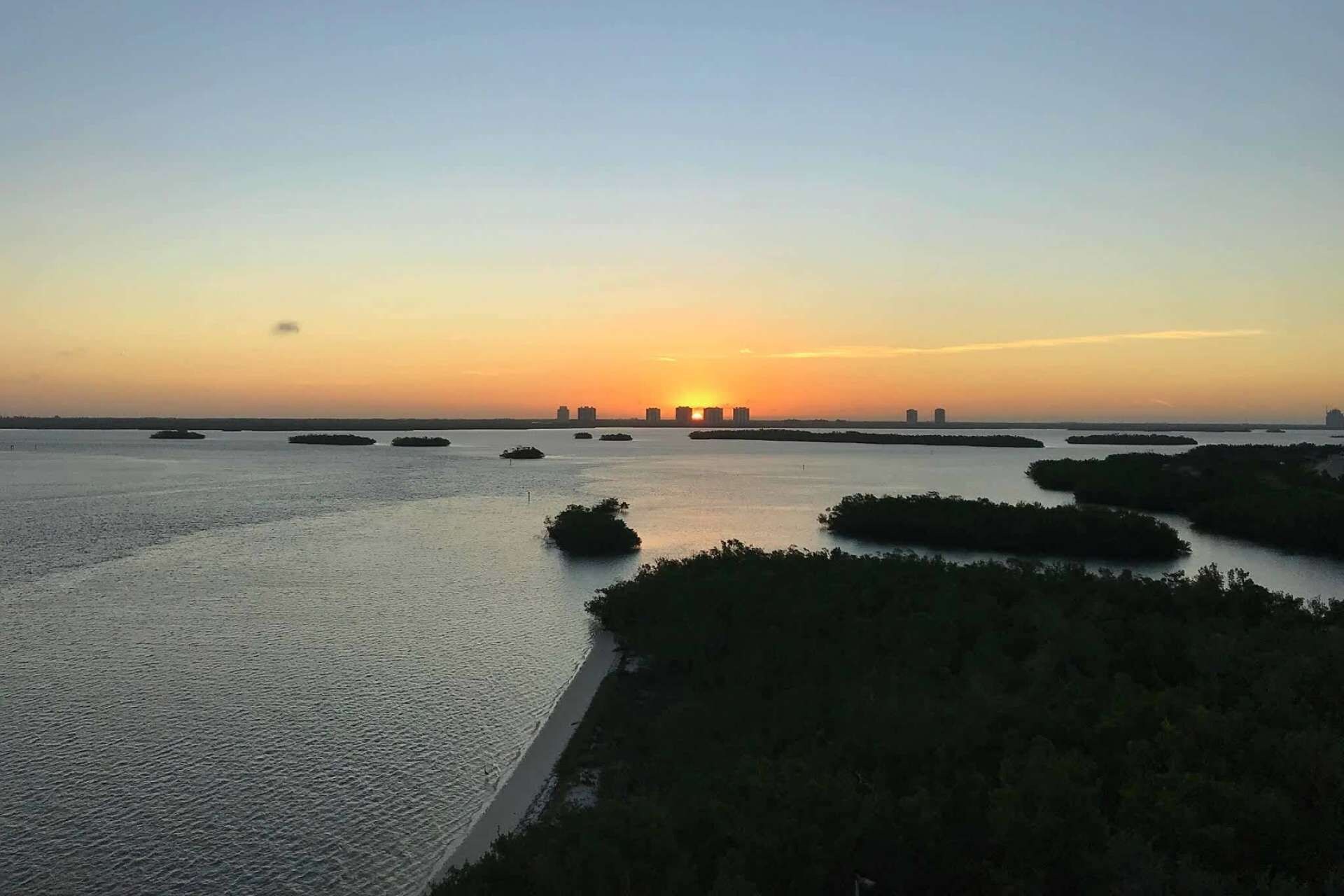 Paisagem costeira com pôr do sol, águas calmas e ilhas espalhadas.
