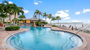 A swimming pool with a 3ft 3in depth, surrounded by palm trees and lounge chairs, with a view of the water and buildings in the background.