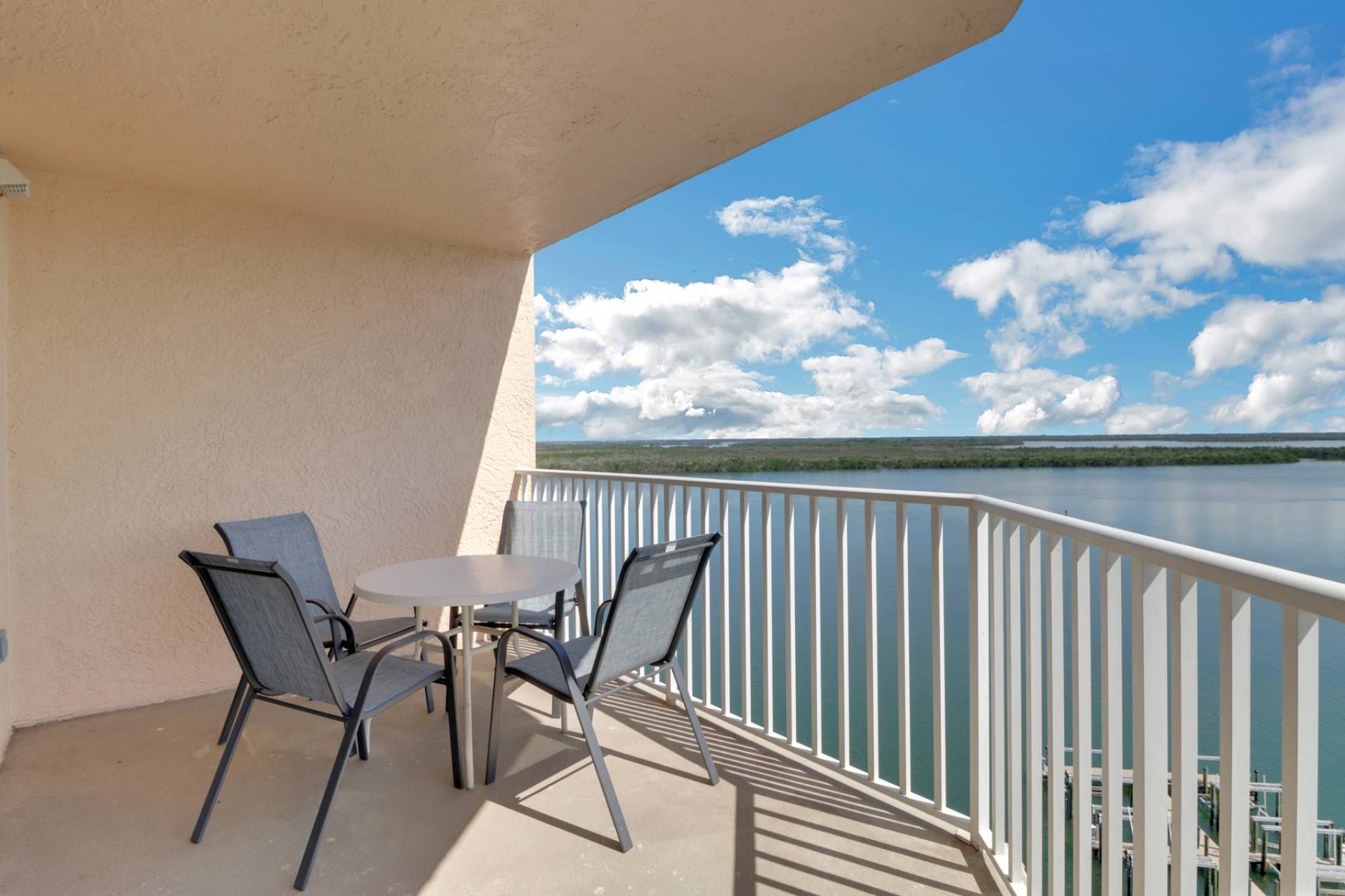 A balcony with a table and chairs, overlooking a calm lake with a distant shoreline.
