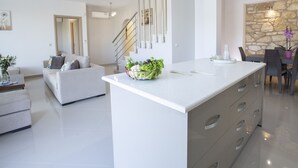 Eine moderne Küche mit Kochinsel, ein Essbereich mit Wandverkleidung aus Stein und ein Wohnzimmer mit Sofa und Treppe.