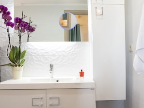 Een badkamer met een wit wastafelmeubel, een spiegel en een potorkidee.