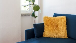 A blue sofa with a yellow fluffy pillow and a green plant beside it. - Experience relaxing holidays (Estoril)