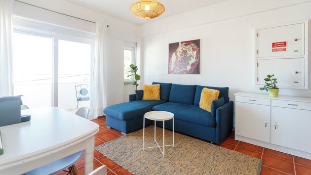 A modern living room with a blue sofa, a small white table, and a patterned rug. - Experience relaxing holidays (Estoril)