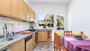 Una cocina compacta con encimeras de granito, armarios de madera y un rincón comedor con una mesa para dos.