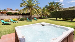 Un jacuzzi en un patio trasero con sillas de jardín verdes y palmeras.