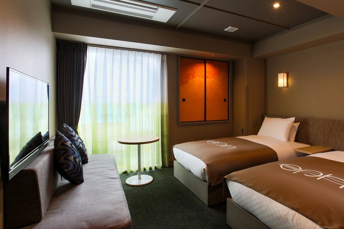 A hotel room with two beds, a sofa, a small round table, and a TV.