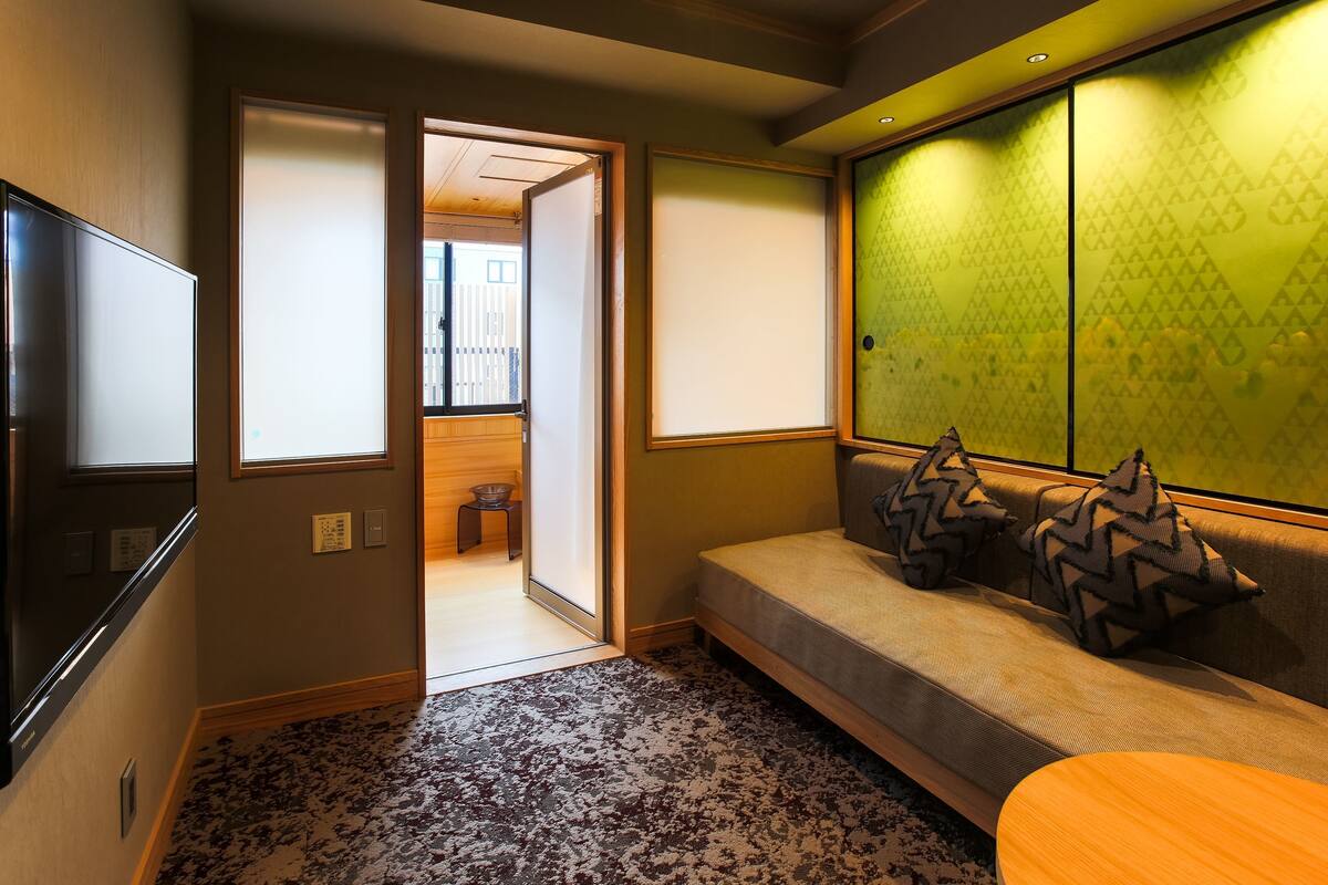 A room with a sofa, a TV, a patterned carpet, and a green partition wall.