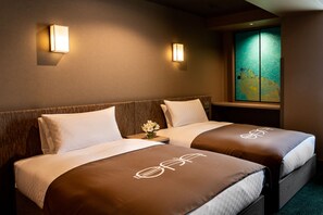 Une chambre d’hôtel avec deux lits, chacun recouvert d’une couverture marron et agrémenté d’un oreiller blanc. Des lampes murales sont fixées de chaque côté des lits, et une fenêtre offre une vue sur le paysage urbain.
