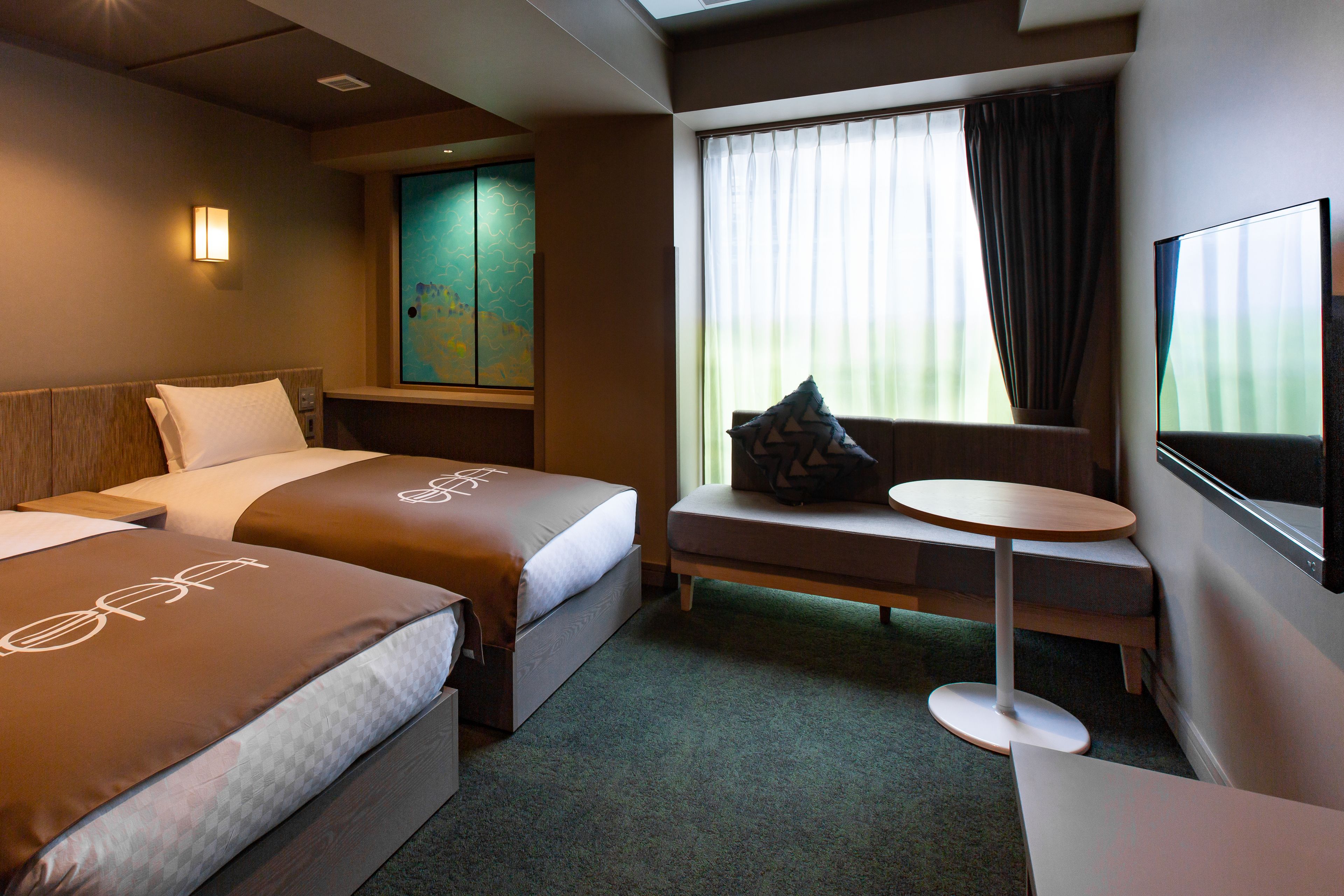 Habitación de hotel con dos camas, una mesita redonda pequeña, un televisor y una ventana con cortinas.