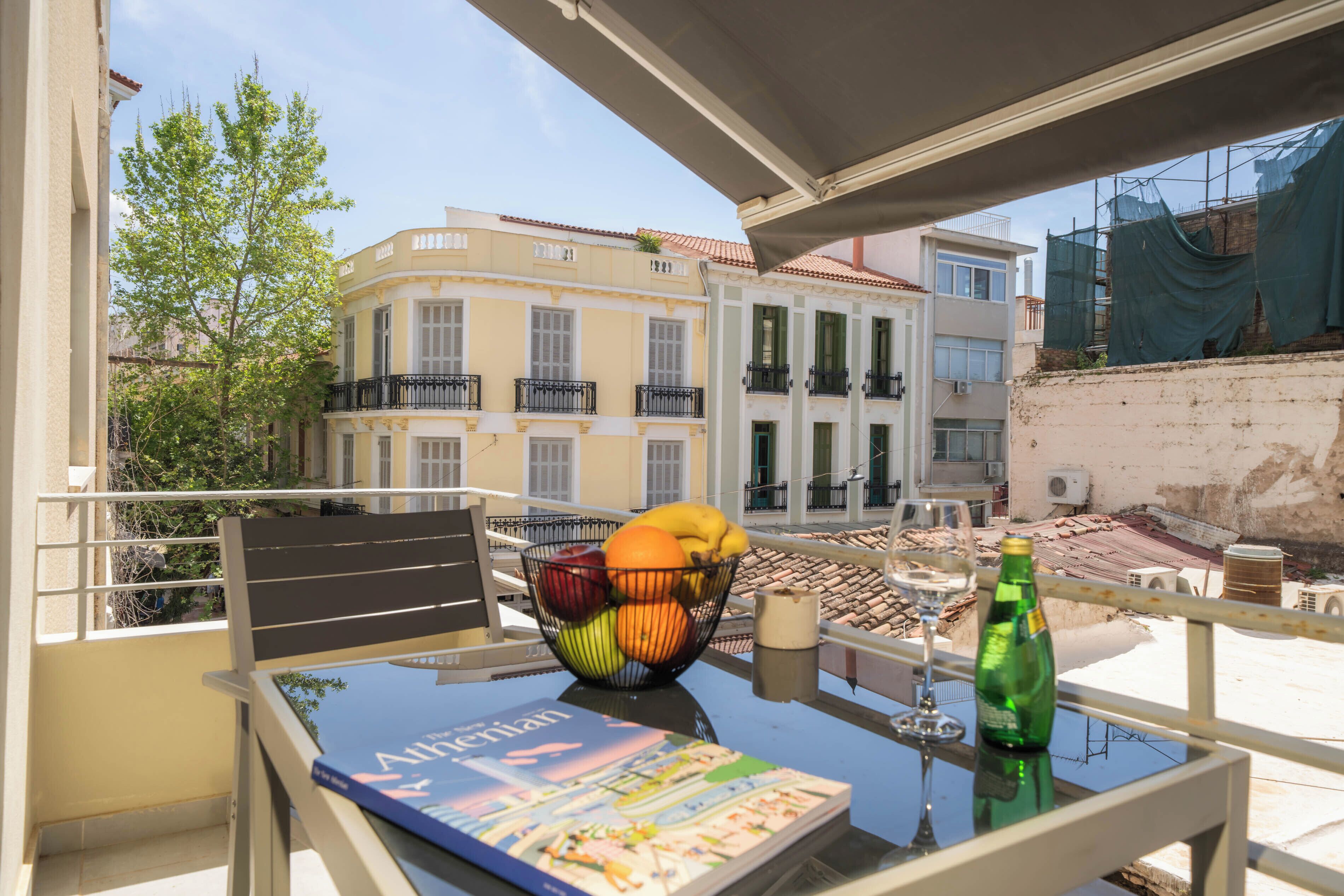 Un balcon avec une table, un panier de fruits, une bouteille et un magazine.