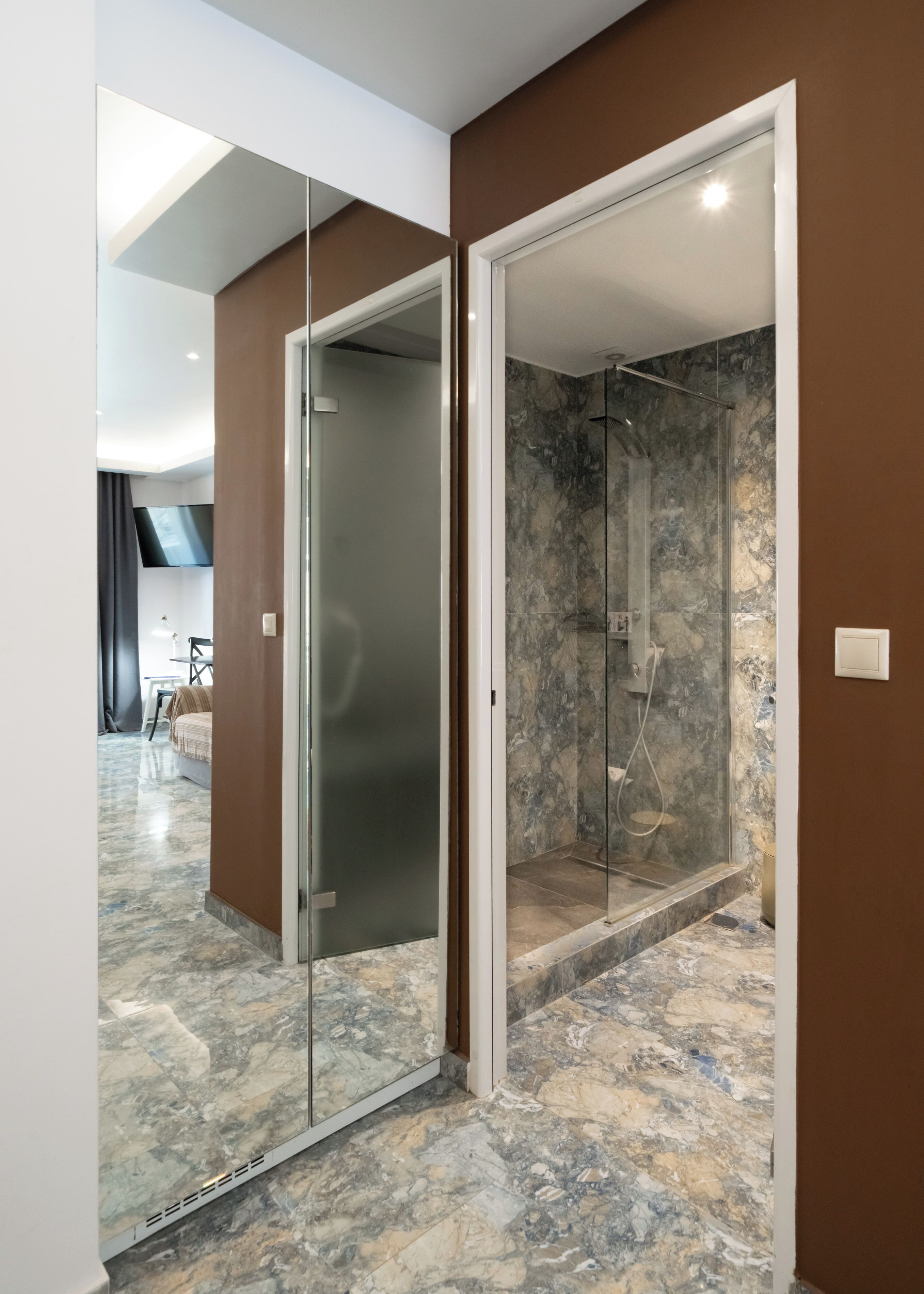 A modern bathroom with a glass-enclosed shower, marble flooring, and a brown accent wall.