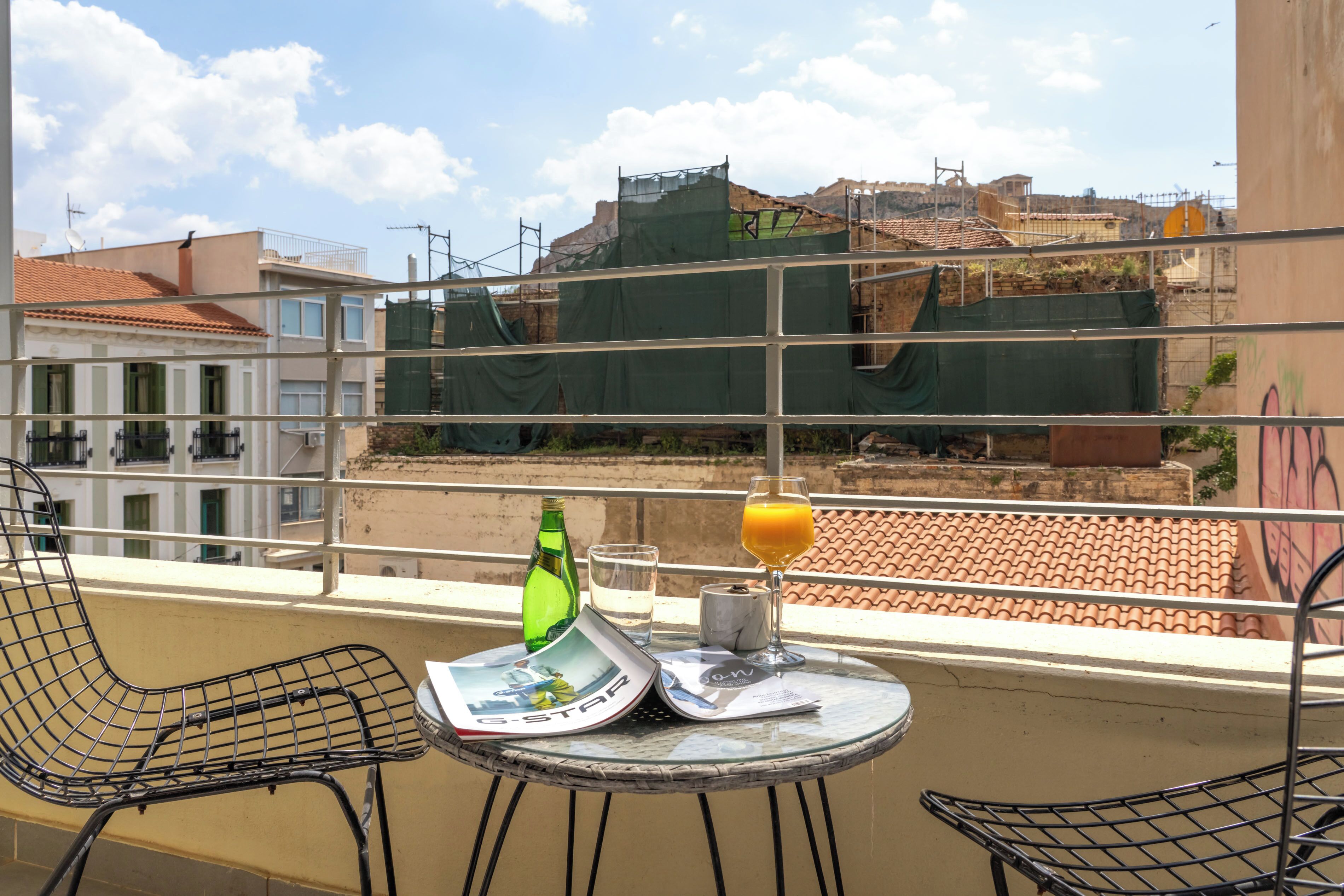 Een balkon met een tafel, stoelen, een fles, een glas jus d'orange en een tijdschrift.