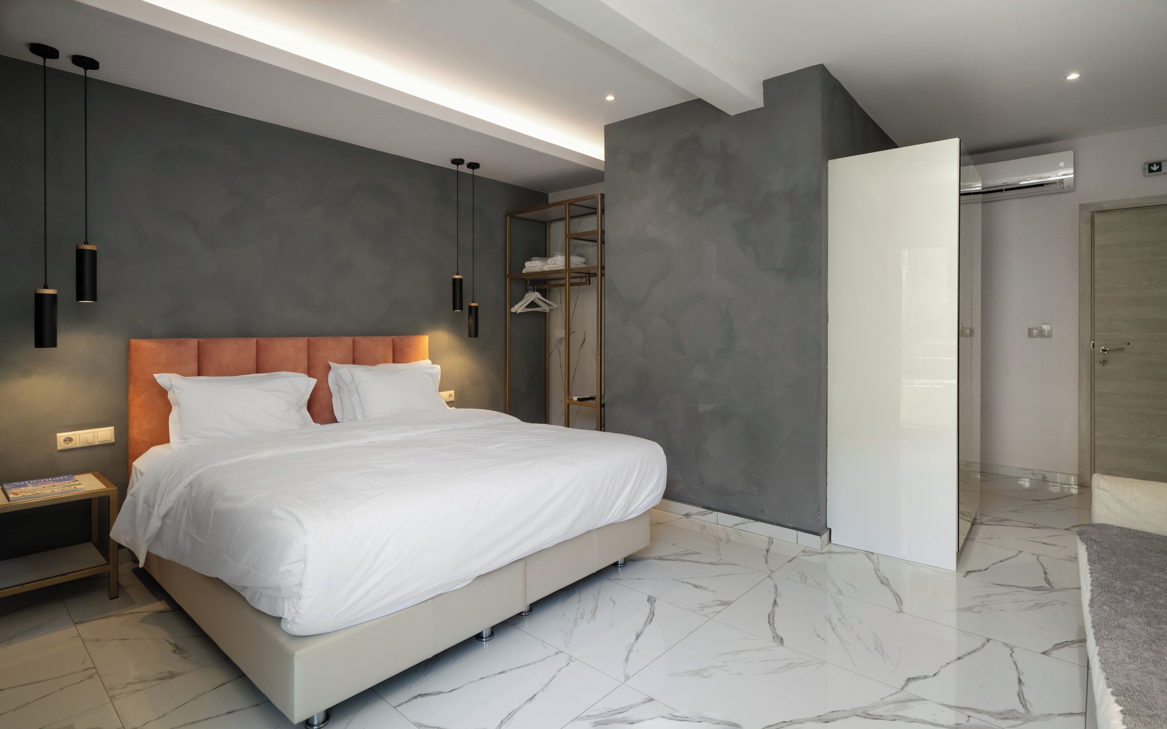 A modern bedroom with a large bed, bedside tables, a wardrobe, and a bathroom with a shower and toilet.