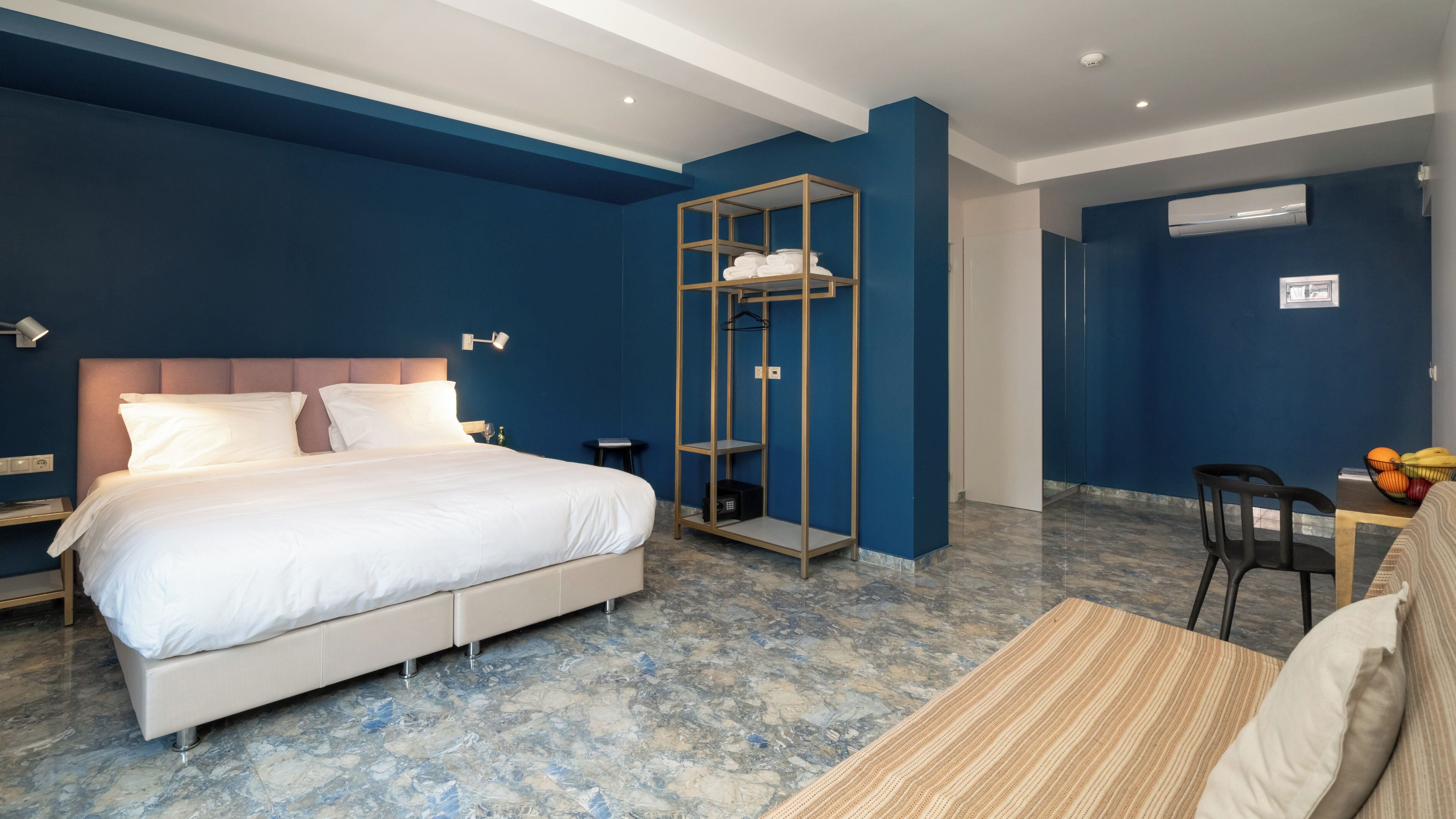 Ein Hotelzimmer mit Bett, Schrank, Schreibtisch mit Stuhl und einem kleinen Tisch mit Obst.