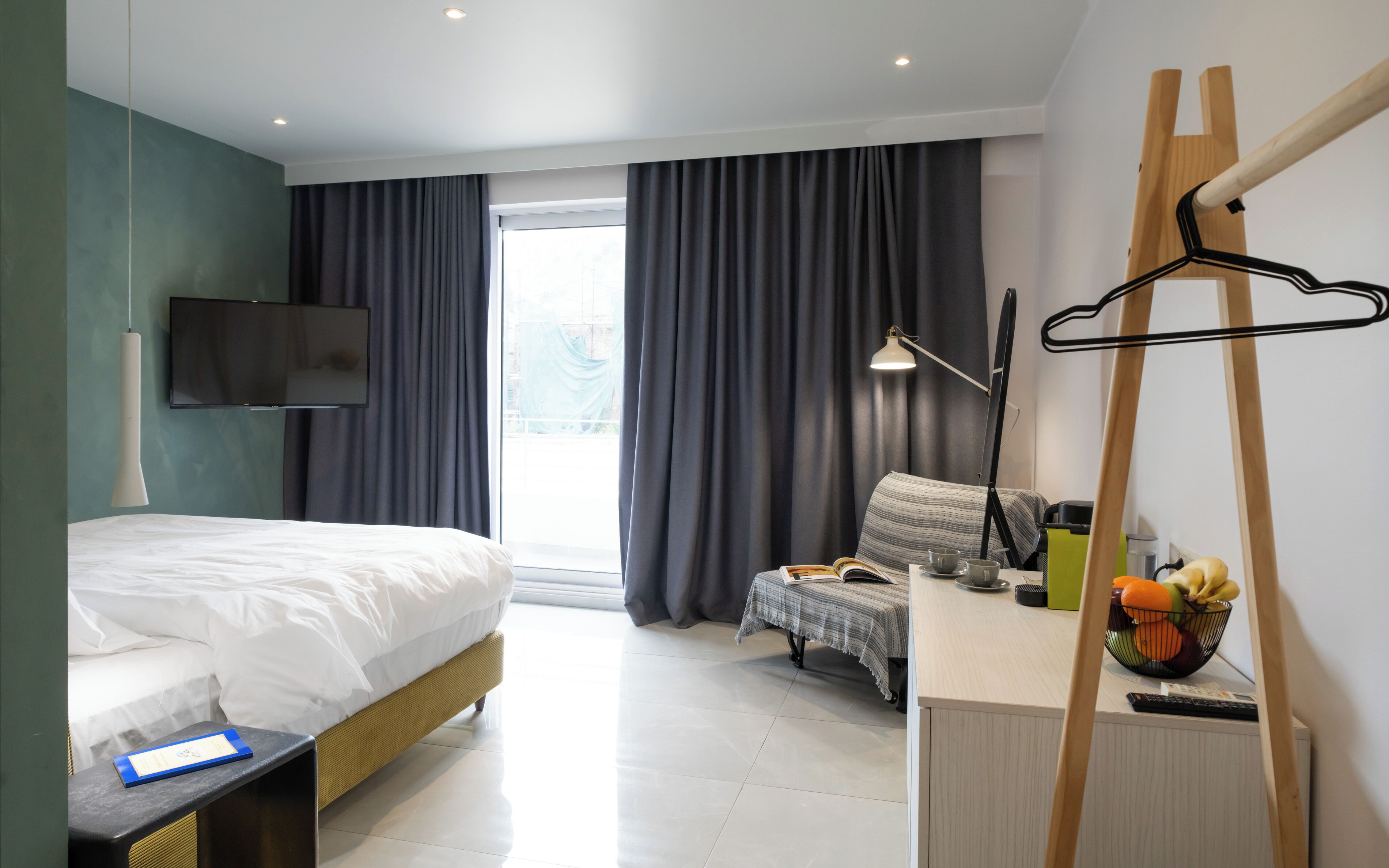 Ein Hotelzimmer mit Bett, Schreibtisch, Stuhl, Fernseher, einem Fenster mit Vorhängen und einem Heizkörper.